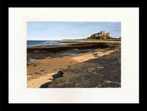 Medieval castle on a grassy hill overlooking a rocky shoreline and calm sea.